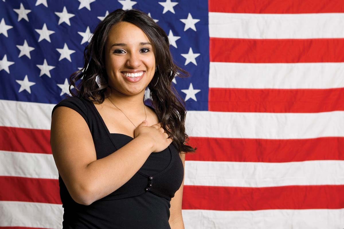 Younger woman with hand over heart in front of American flag