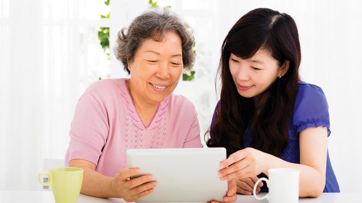 Smiling older and younger women holding tablet at table in bright home
